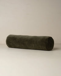 The Saarde Velvet Structured Bolster in Dark Olive rests on a plain, light surface against a neutral wall.