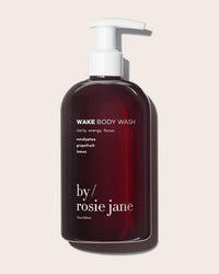 A dark amber pump bottle labeled "Wake Body Wash" by Rosie Jane, an antioxidant-rich body wash with eucalyptus, grapefruit, and lemon notes, features white text on a light background.