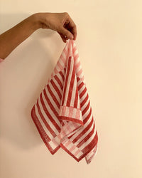 A hand holds up the Casa Amarosa Stripe Hand Block Printed Scarf in Red & Pink against a plain beige wall.