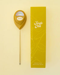 A green Jungle Club Moisture Meter serves as a reliable watering indicator, shown next to its matching box on a light yellow background. The device features a dial labeled Moist and Met for easy moisture readings.