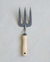 The Floral Society's Forged Fork, featuring a light wooden handle and crafted from boron steel, is shown on a light gray textured surface.