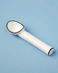 The Be Home US Harlow Ice Cream Scoop, featuring white ceramic with black trim and vintage style, rests on a light blue surface.