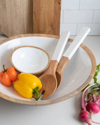 The Madras Serving Set in White by Be Home US includes a large white bowl with wooden edges, a handcrafted mango wood serving set, a smaller bowl, and two salad servers. Radishes and greens sit nearby on the counter.