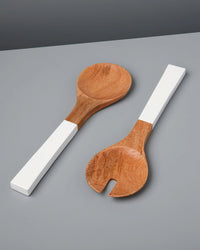 The Madras Serving Set in White by Be Home US features two mango wood salad servers with white rectangular handles, placed on a flat gray surface for an heirloom-quality and timeless look.
