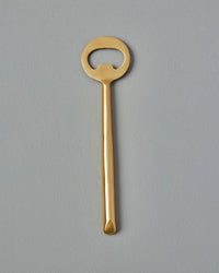 The Be Home US Matte Gold Bottle Opener features a round handle and matte finish, shown against a gray background—an ideal addition to your barware collection.