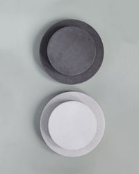 Two 13.8-inch Rolling Stone Plant Trolleys in grey terrazzo by Bergs Potter, one in dark and one in light gray, are paired on a plain, light gray background, showcasing their sleek terrazzo-inspired design.