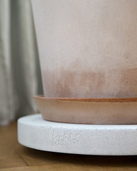 Close-up of a beige Bergs Potter flowerpot with matching saucer on a 9.8 inch Rolling Stone Plant Trolley in White Terrazzo by Bergs Potter, featuring the brands label.