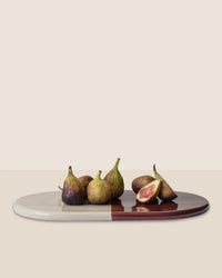 Six figs, one sliced, are displayed on the Nuna Glazed 13.4 x 7.9 Tray in Sandstone/Deep Burgundy by Bergs Potter. This elegant, food-safe stoneware piece pairs beautifully with Nuna Coasters against a neutral backdrop.