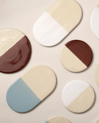 The Bergs Potter Nuna Glazed 7.9 inch Tray in Sandstone/Deep Burgundy features a two-tone round stoneware design, food safe for easy dining, and is shown arranged on a neutral background with other assorted plates.