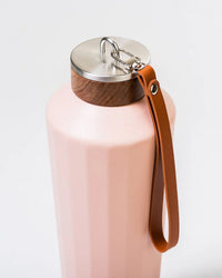 The 25oz Hemingway Flask in Dusty Pink by Business & Pleasure Co features a textured design, metal and wood lid, brown leather strap on the cap, and vacuum insulation to keep drinks perfectly hot or cold.