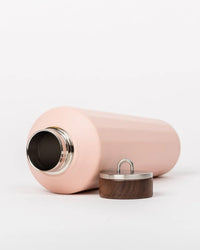 A 25oz Hemingway Flask in Dusty Pink by Business & Pleasure Co lies on its side, with its metal and wood lid placed beside the opening, set against a plain white background.