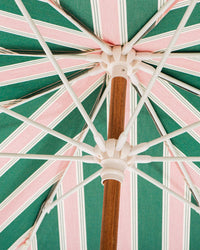 Enjoy shade under the Amalfi Umbrella - Bistro Green Stripe by Business & Pleasure Co, featuring green and white panels, a wooden central pole, and white support ribs—all offering UV protection in Mediterranean style.