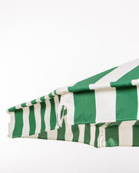 A close-up of the Business & Pleasure Co Amalfi Umbrella - Crew Canyon Green Stripe features a green and white striped, UV-resistant canopy with taut fabric and gently scalloped edges, set against a plain white background.