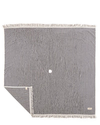 The Beach Blanket - Laurens Navy Stripe by Business & Pleasure Co is a family-friendly, square black and white striped 100% cotton blanket with fringed edges, a small white circle in the center, and a corner folded to reveal the reverse side.