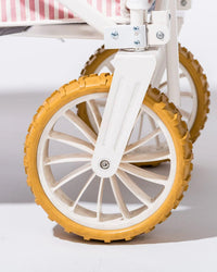 Close-up of the Beach Cart - Laurens Pink Stripe by Business & Pleasure Co, showing its white wheel with a yellow sand tire, attached to a white metal frame and pink-and-white striped fabric above.