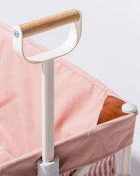 A close-up of the wooden-grip handle on a metal pole, beside the Laurens Pink Stripe Beach Cart by Business & Pleasure Co, featuring light pink fabric, striped inner lining, and a compact foldable design.