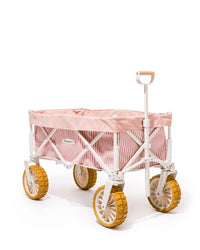 The Beach Cart - Laurens Pink Stripe by Business & Pleasure Co features a compact, foldable design with pink and white striped fabric, a white frame, and large yellow sand wheels, shown against a white background.