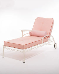 A white metal outdoor chaise lounge with pink cushions and the Business & Pleasure Co Bolster Pillow – Laurens Pink Stripe, featuring spill, stain, and fade resistance, shown on a plain white background.