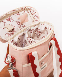 The Wine Cooler Tote Bag - Rivie Pink by Business & Pleasure Co is a pink canvas bag with a red and white strap, insulated interior, and a red nature-inspired lining—perfect for carrying wine in style.