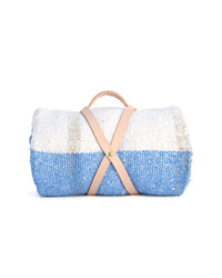 The Suave Aire - Blanket Roll by caminito is a handwoven indoor/outdoor blanket in blue, white, and beige, secured with a tan leather strap and handy handle. Displayed against a white background.