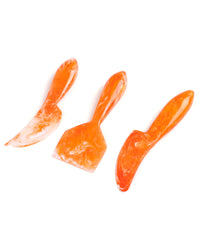 The Casa Amarosa Resin Cheese Knife Set of 3 in Orange features orange and white marbled knives with varied blade shapes, displayed on a white background.