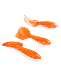 Three orange marbled utensils—a spoon, spatula, and spreader—are displayed on white, highlighting Casa Amarosa’s Resin Cheese Knife Set of 3 in Orange, ideal for serving or elevating any charcuterie board with handmade style.