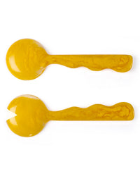 The Casa Amarosa Resin Salad Server Set in Mustard features two handmade servers—one spoon and one V-notched—both with curved handles and a marbled yellow texture, displayed side by side on a white background.