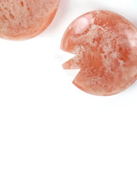 Two round, pink resin objects from the Casa Amarosa Resin Short Salad Server Set rest on a white surface; one features a wedge-shaped notch, echoing the elegant curves typical of handmade salad servers.