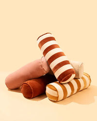 Five Casa Amarosa Velvet Bolster Pillows in Pink are stacked together—three in solid pink or reddish-brown and two with brown and white stripes—ideal cotton velvet accents for luxe home décor.