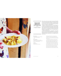 A person holds a white plate of pasta with the cover of Pasta Grannies: The Official Cookbook by Chronicle Books, inspired by Italian grandmothers, shown against a wooden background. Recipe text appears on the right side.