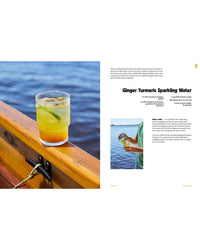 A glass of ginger turmeric sparkling water with ice and lime is pictured on a wooden railing by the water; another image shows someone pouring the drink. Recipe text, inspired by Chronicle Books Sea Lovers Cookbook, appears on the right.