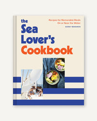 The cover of Sea Lovers Cookbook by Chronicle Books displays bold blue and orange text, photos of a sailboat and seafood dishes, and blue stripes along the bottom.