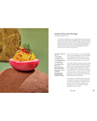 A halved pink deviled egg with smoked salmon filling, dill, and roe sits on a brown surface. Inspired by tinned fish recipes from Tin to Table by Chronicle Books, the recipe text is shown on the right.