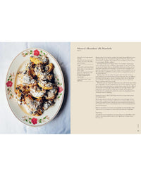 A floral plate with almond pastries dusted in powdered sugar sits beside a recipe from Wild Figs and Fennel by Chronicle Books, displayed on a beige background.
