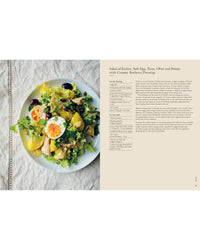 A plate of salad with endive, soft-boiled eggs, tuna, potatoes, black olives, and greens sits beside a recipe page from Chronicle Books’ Wild Figs and Fennel on a beige background.