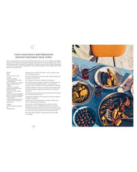 A table set with Mediterranean vegetables, olives, bread, and water sits beside an open copy of Yiayia by Chronicle Books, featuring delicious regional Greek cookery and vegetarian dishes.