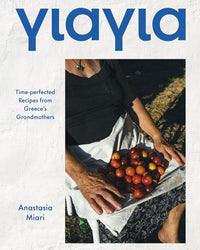 A woman in a black top and white apron holds red tomatoes on the cover of Yiayia by Chronicle Books, which features time-perfected recipes from Greece’s grandmothers and celebrates regional Greek cookery.
