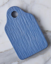 The etúHOME Dutch Small Cheese Board w/ Spreader in Denim Blue rests on a white marble surface.
