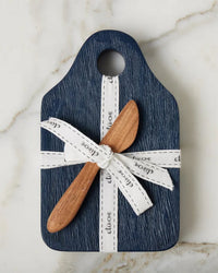 The etúHOME Dutch Small Cheese Board w/ Spreader in Navy Blue features a top hole with a white ribbon and includes a wooden spreader, all elegantly displayed on a marble surface.