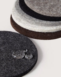 A close-up of stacked graf lantz Bierfilzl Merino Wool Felt Round Coaster Multi in Earth (6 Pack), made from sustainable German Merino wool, with water droplets on top—ideal for eco-friendly home décor.