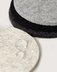 Close-up of three graf lantz Bierfilzl Merino Wool Felt Round Coasters Multi in Noir (4 Pack) in light and dark gray, with water droplets on the front—an elegant, sustainable addition to your home decor.
