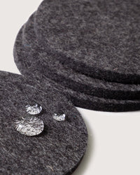 Four round charcoal Bierfilzl Merino Wool Felt Coasters by graf lantz are stacked, with three clear water droplets on the top—an elegant, sustainable touch for your home decor.