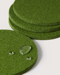 Four Loden Green Bierfilzl Merino Wool Felt Round Coasters by graf lantz are stacked, with one in front displaying three water droplets—showcasing the classic 4-pack style.