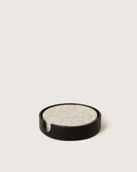 A stack of light grey felt coasters rests in the graf lantz Kobon Leather Round Tray in Black, which doubles as a sleek holder and stylish catch-all on a plain light surface.