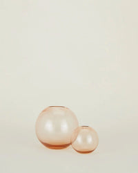 Two Aurora Sphere Vases in Blush by Hawkins New York, featuring handblown translucent glass, are displayed side by side against an off-white background, capturing the gentle glow of the Northern Lights.