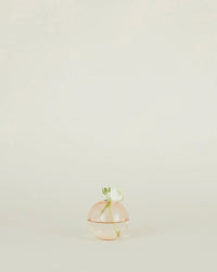 The Aurora Sphere Vase in Blush by Hawkins New York, a round translucent pink handblown glass piece with a green leaf and stem detail, is displayed centered on a plain light background.