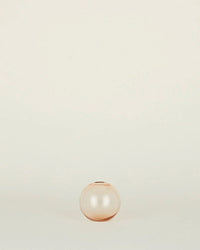 The Aurora Sphere Vase in Blush by Hawkins New York, a small round handblown light pink glass vase, sits centered on a plain off-white background.