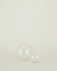Two clear Aurora Sphere Vases by Hawkins New York, crafted from recycled handblown glass in different sizes, are arranged side by side on a plain, light background.