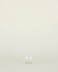 The Aurora Sphere Vase in Clear by Hawkins New York, crafted from recycled handblown glass, sits centered on a light surface with a neutral background.