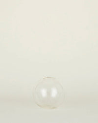 The Aurora Sphere Vase in Clear by Hawkins New York, crafted from recycled handblown glass, sits centered empty on a plain light background.